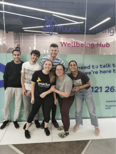 Young people huddling outside the entrance of the Mind Birmingham hub smiling in a group photo s