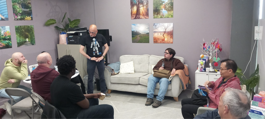 Men in a grey room with calming imagery of nature around them, sitting together and discussing something.