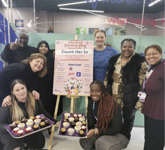 Group photo of ladies around a poster that says 'Count her in', smiling in a group photo and raising money with cupcakes